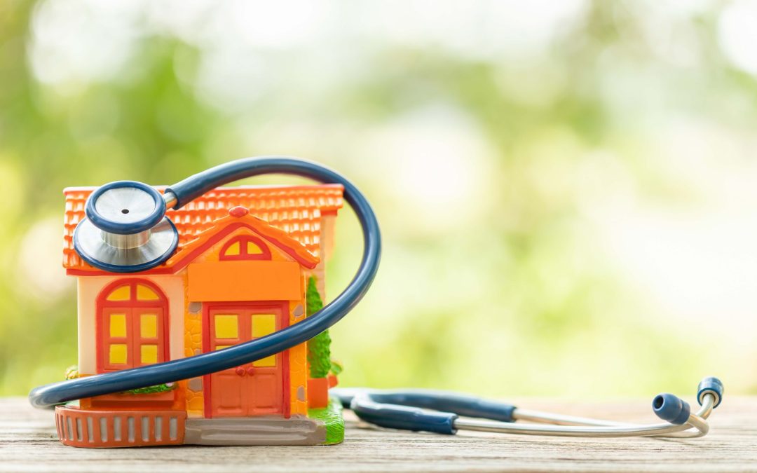 Hand holding blue stethoscope and orange house model on wooden t